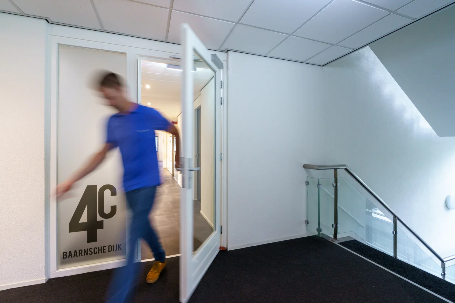 Een man loopt door een open deur met het opschrift "4C Baarnsche Dijk" in een kantoorpand.